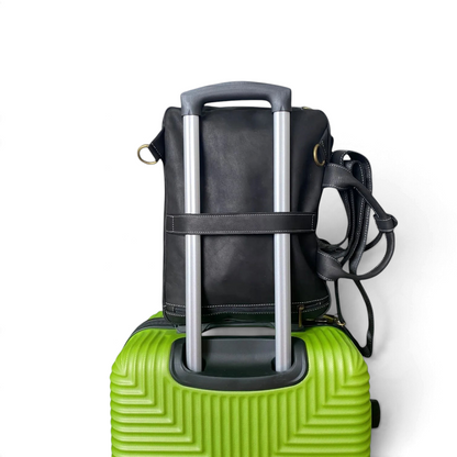 Borsa zaino Amatì Ares Mini in pelle nera fissata al manico di un trolley verde per il trasporto in viaggio
