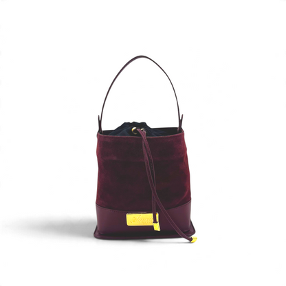 Borsa a secchiello Amatì bordeaux in camoscio con chiusura a coulisse, manico e placca metallica dorata frontale.
