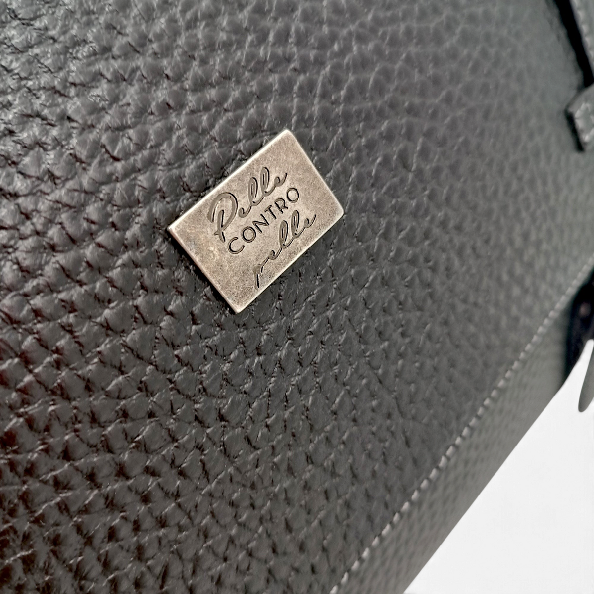 Dettaglio della borsa messenger Amatì Hermes in pelle bucciata nera con targhetta metallica del brand